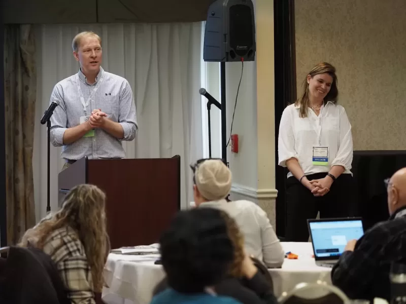 Photograph of VTVLC director, Greg Runyan, and VTVLC Assistant Director Ashley Newton, standing at a podium in a banquet room before an audience of OBLC.