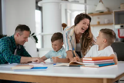 parents laugh with children while working on homework Parents laugh with children while they work on homework at a kitchen table containing books.