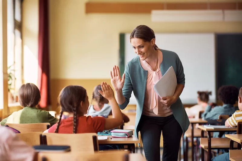 teacher giving high-five to her student Happy elementary school teacher giving high-five to her student during class in the classroom.